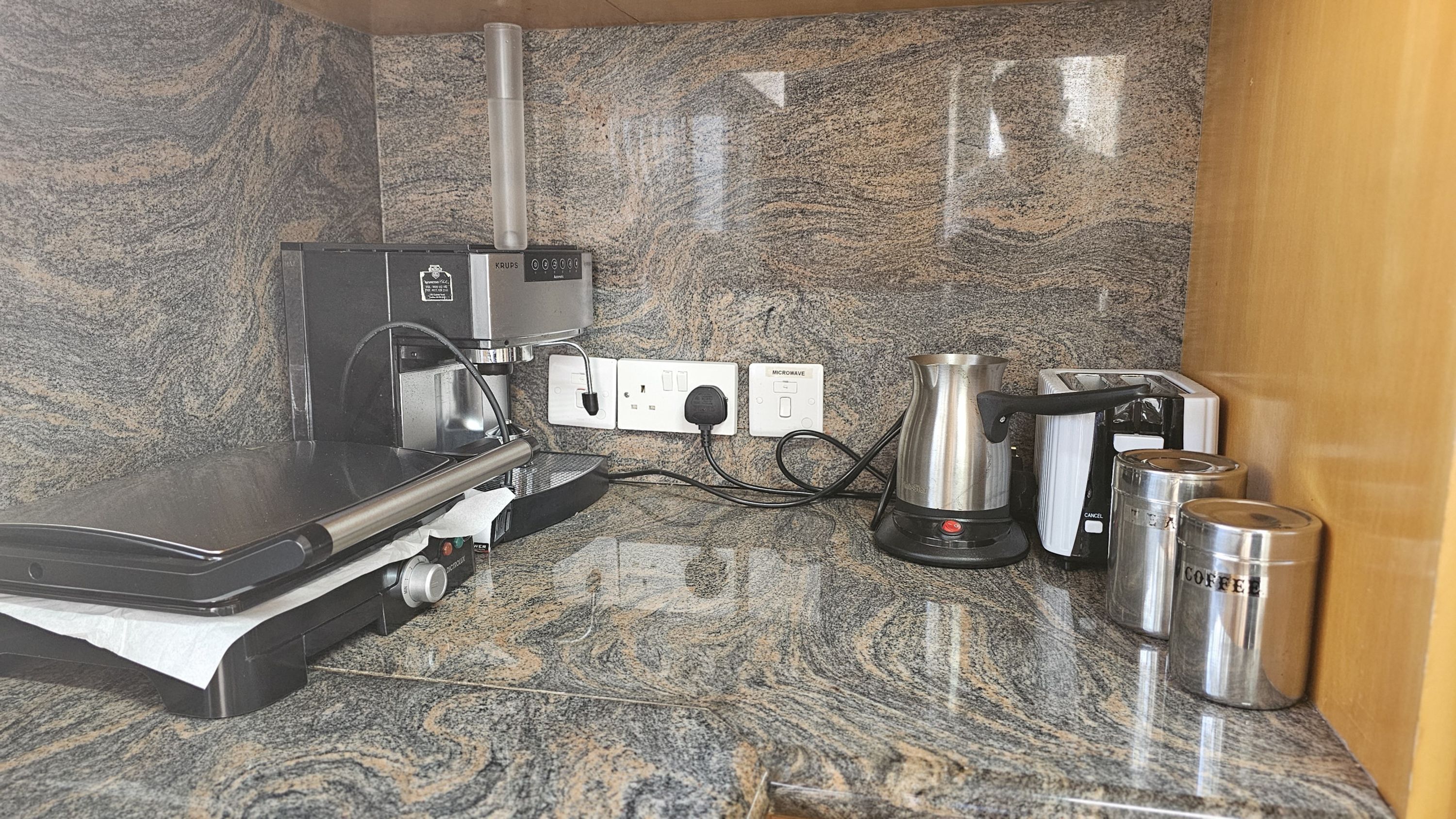 Una cocina con cafetera, hervidor y tostadora sobre una encimera de granito.