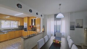A modern kitchen with wooden cabinets, a built-in oven, and a dining area with a table and chairs. - 124 PRO - Stay Princess Villa (Paralimni)