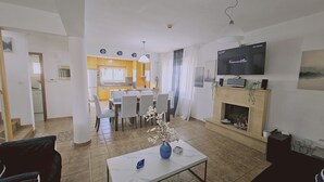 A living room with a TV, a fireplace, and a dining area in the background. - 124 PRO - Stay Princess Villa (Paralimni)