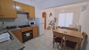 Una cocina compacta con armarios de madera, un microondas, una estufa y un refrigerador. Hay una zona de comedor con una mesa y sillas.