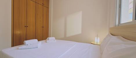 Une chambre d’hôtel avec une grande armoire en bois, un lit bien fait avec du linge de lit blanc et une table de chevet avec une lampe.