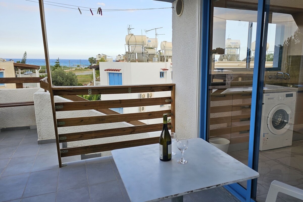 A balcony with a table, a bottle, and a glass. There is a washing machine visible through the glass door.