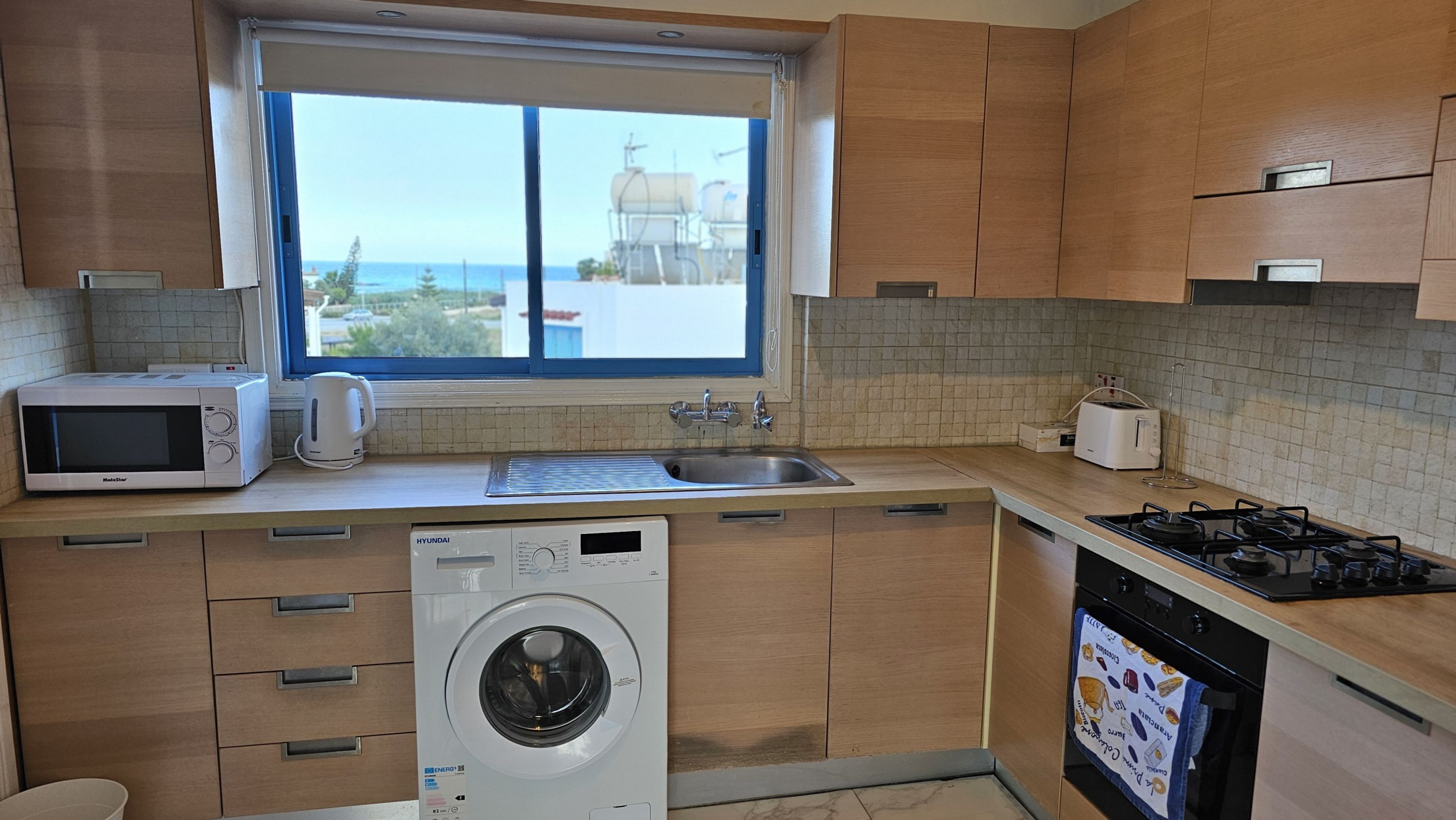 A modern kitchen with wooden cabinets, a built-in microwave, a sink, a washing machine, and a dishwasher.