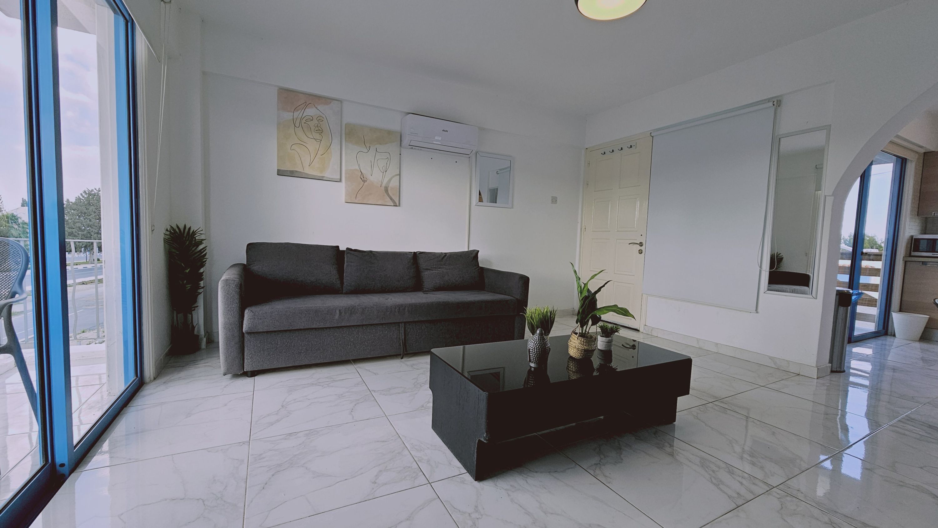 A modern living room with a grey sofa, a black coffee table, and a large window offering a view of the outdoors.