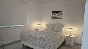 A neatly arranged bedroom with a bed, two bedside tables, a wall-mounted artwork, and a window with blinds. - 145 NIC - Stay Historia Apartment (Nicosia)