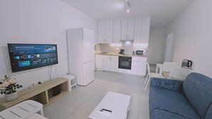 A modern living room with a flat-screen TV, a blue sofa, a coffee table, and a small white table with a plant. - 145 NIC - Stay Historia Apartment (Nicosia)