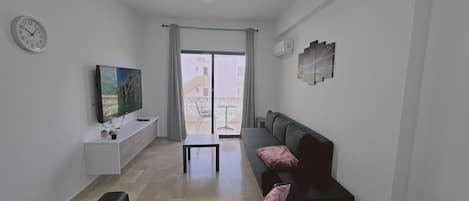 Un salon équipé d’un téléviseur à écran plat, d’un canapé, d’une table basse et d’une porte-fenêtre coulissante donnant sur un balcon.