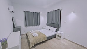 A modern bedroom with a bed, bedside tables, a nightstand, and a wall-mounted air conditioner. - 117 KPF - Stay Tranquil Haven (Paphos)