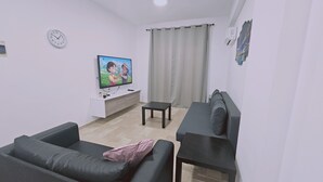 A living room with a flat-screen TV, a sofa, a small table, and a grey couch. - 117 KPF - Stay Tranquil Haven (Paphos)