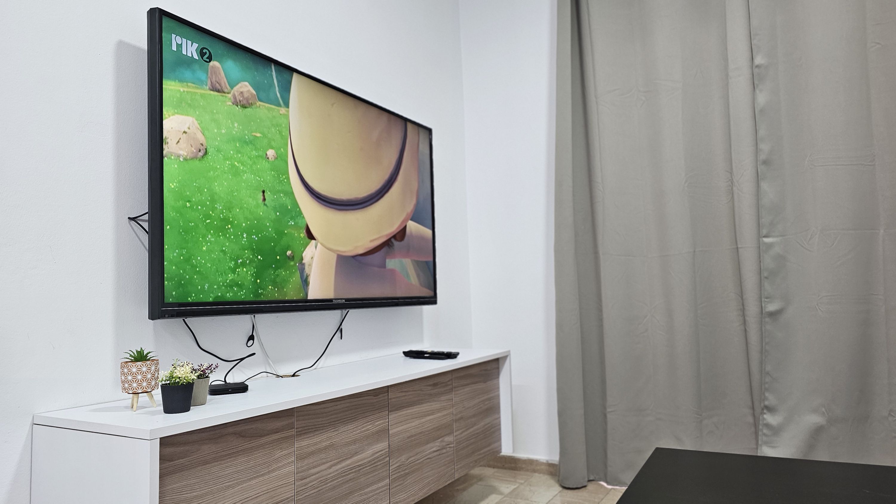 A flat-screen TV mounted on a white wall, with a wooden cabinet below.