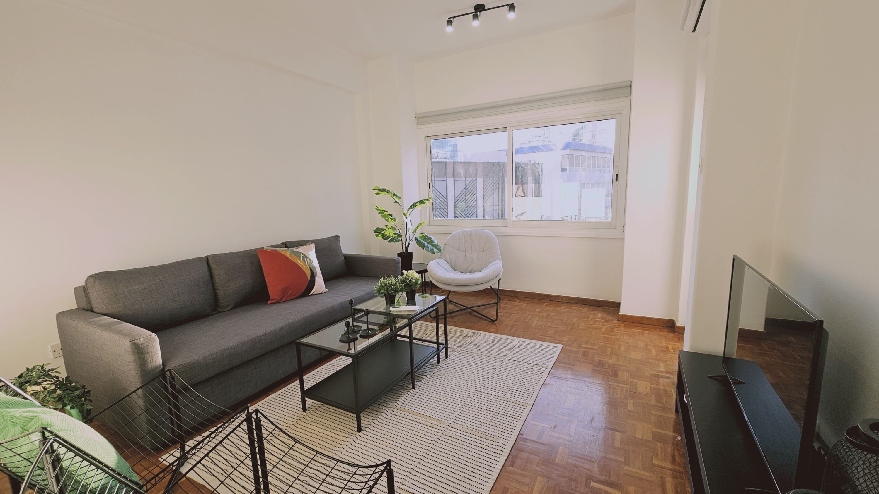 A modern living room with a grey sofa, a white armchair, a glass coffee table, and a TV stand.