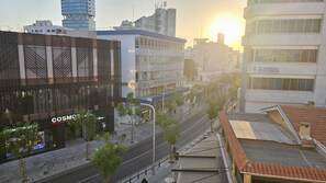 Une rue de la ville bordée de bâtiments modernes, dont un magasin COSMOS, et offrant une vue dégagée sur le soleil couchant à l’horizon.