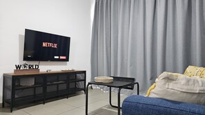 A modern living room with a flat-screen TV on a wooden stand, a black mesh entertainment unit, a small black table with a woven basket, and a grey curtain. - 135 PRO - Stay Arpa Suite (Paralimni)