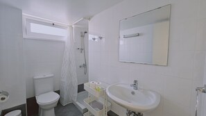A bathroom with a toilet, shower, sink, and a window.
