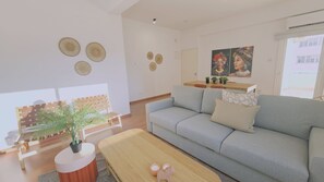 Ein modernes Wohnzimmer mit einem grauen Sofa, einem Holztisch und einer kleinen Pflanze. An den Wänden befinden sich Wandbehänge und ein Gemälde.