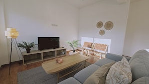 Ein modernes Wohnzimmer mit Flachbildfernseher, Holztisch, grauem Sofa und zwei Zimmerpflanzen.