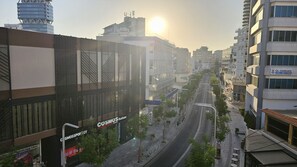 A city street with modern buildings, including a Cosmosporty store, and a clear view of the sun setting in the distance.