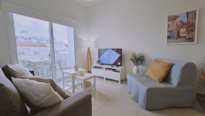 Un salon moderne avec un canapé, un téléviseur posé sur un meuble, une petite table et un balcon offrant une vue sur les immebles.