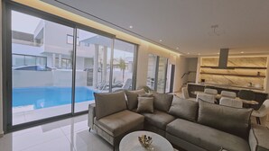 A modern living room with a large sectional sofa, a dining area with a round table, and a kitchen with marble countertops. - 146 4 AN - Stay Oasis Luxury Villa (Ayia Napa)