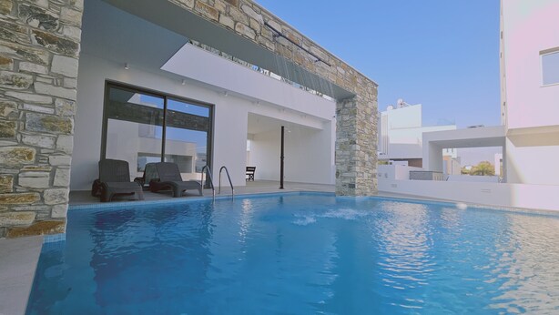 A modern pool area with stone walls, a clear blue pool, and lounge chairs. - 146 4 AN - Stay Oasis Luxury Villa (Ayia Napa)