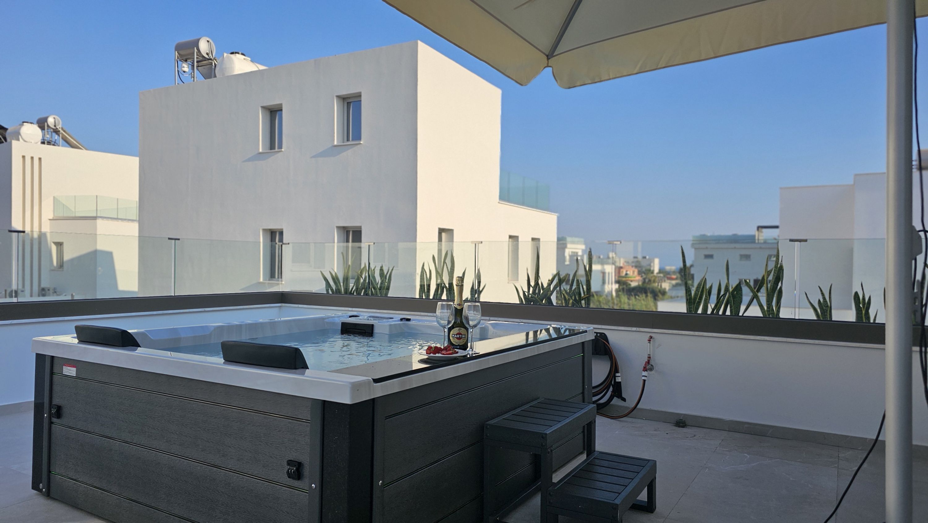 A rooftop terrace with a hot tub, a bottle of champagne, and a glass.