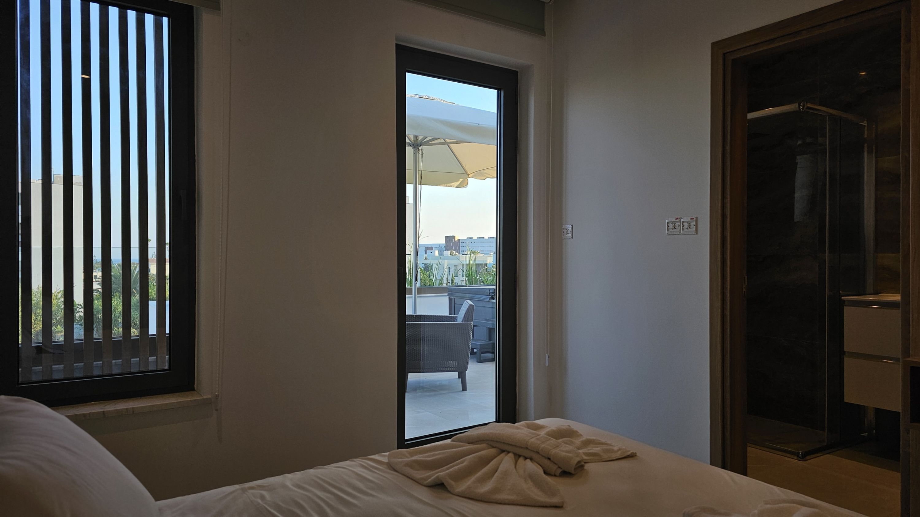 Une chambre à coucher avec un lit, une fenêtre avec des stores, une porte donnant sur un balcon et une armoire.