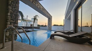 Un espace piscine moderne agrémenté de piliers en pierre, de chaises longues et offrant une vue dégagée sur les bâtiments environnants.