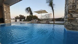 Une piscine entourée de chaises longues et d’un parasol, le tout bordé de murs en pierre et d’une clôture.