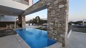 Une piscine avec des murs en pierre, des meubles d’extérieur et une vue sur la rue.