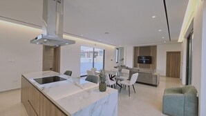 Una cocina moderna con una isla de mármol, comedor con sillas y un televisor montado en la pared.