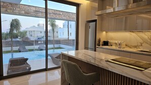 Cocina moderna con una isla grande, pared de piedra y vista a una piscina y zona de estar exterior.