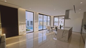 A modern kitchen with a marble countertop, a dining area with a glass table, and a view of a swimming pool through large sliding doors. - 146 5 AN - Stay Oasis Luxury Villa (Ayia Napa)