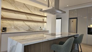 Une cuisine moderne dotée d’un plan de travail en marbre, d’appareils électroménagers en acier inoxydable et d’une cuisinière intégrée.