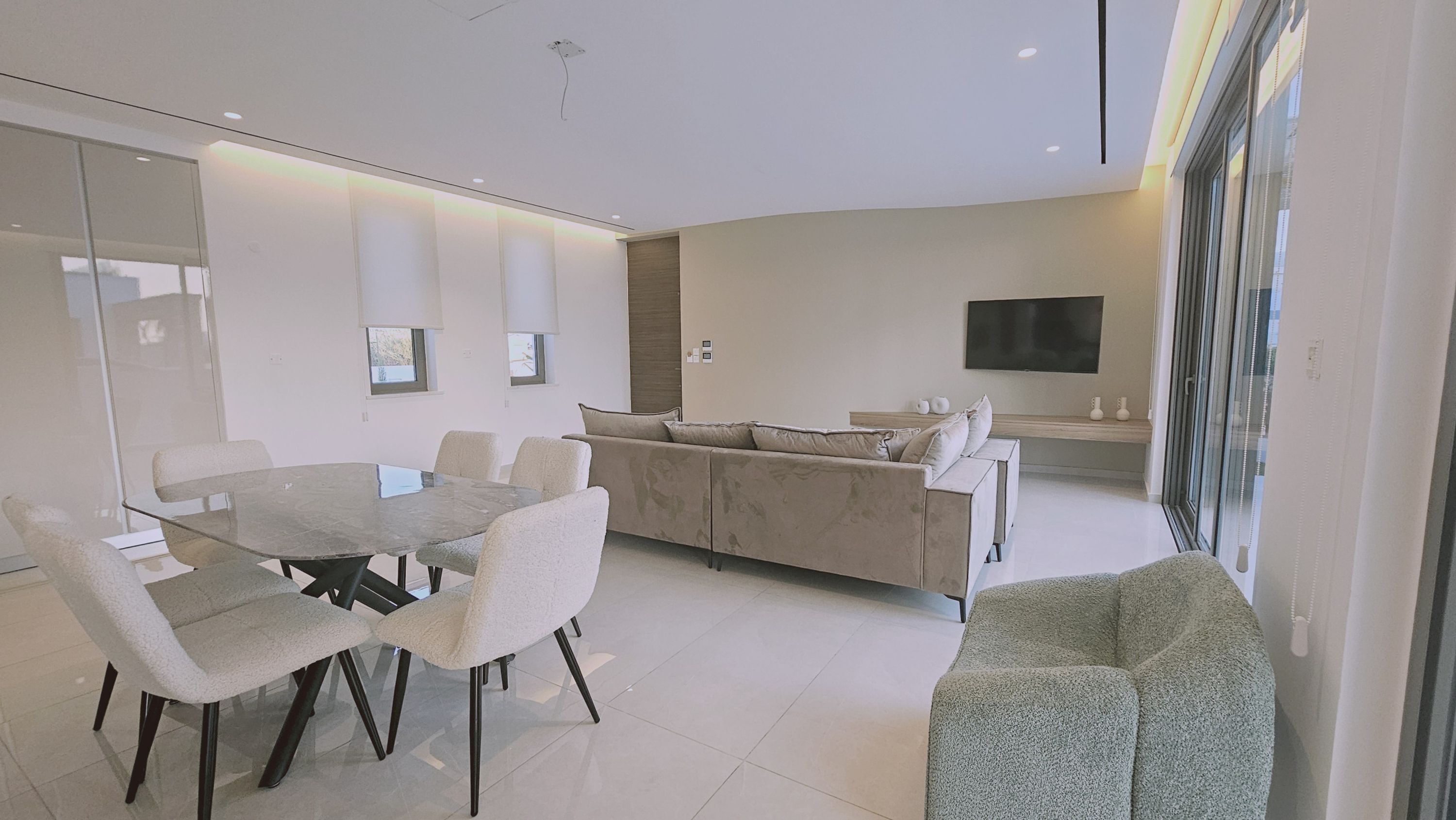 A modern living room with a glass dining table, a beige sofa, and a grey armchair.