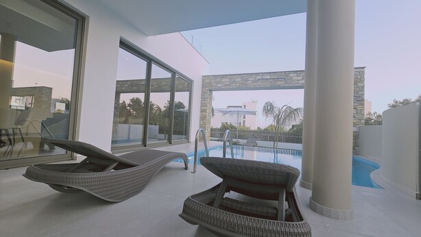 Un espace piscine extérieur moderne, doté de deux fauteuils de relaxation en osier, offrant une vue dégagée sur la piscine et adossé à un mur en pierre.