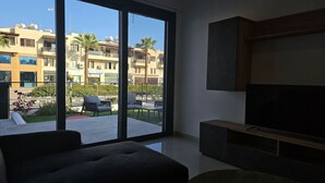 A modern living room with a large TV, a sofa, and a balcony with outdoor furniture.