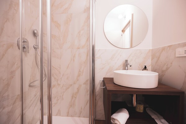 A bathroom with a glass-enclosed shower, a round mirror, and a wooden vanity with a white sink.
