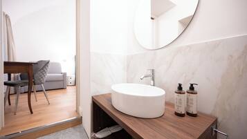 A modern bathroom with a round sink, a mirror, and two bottles of shampoo.