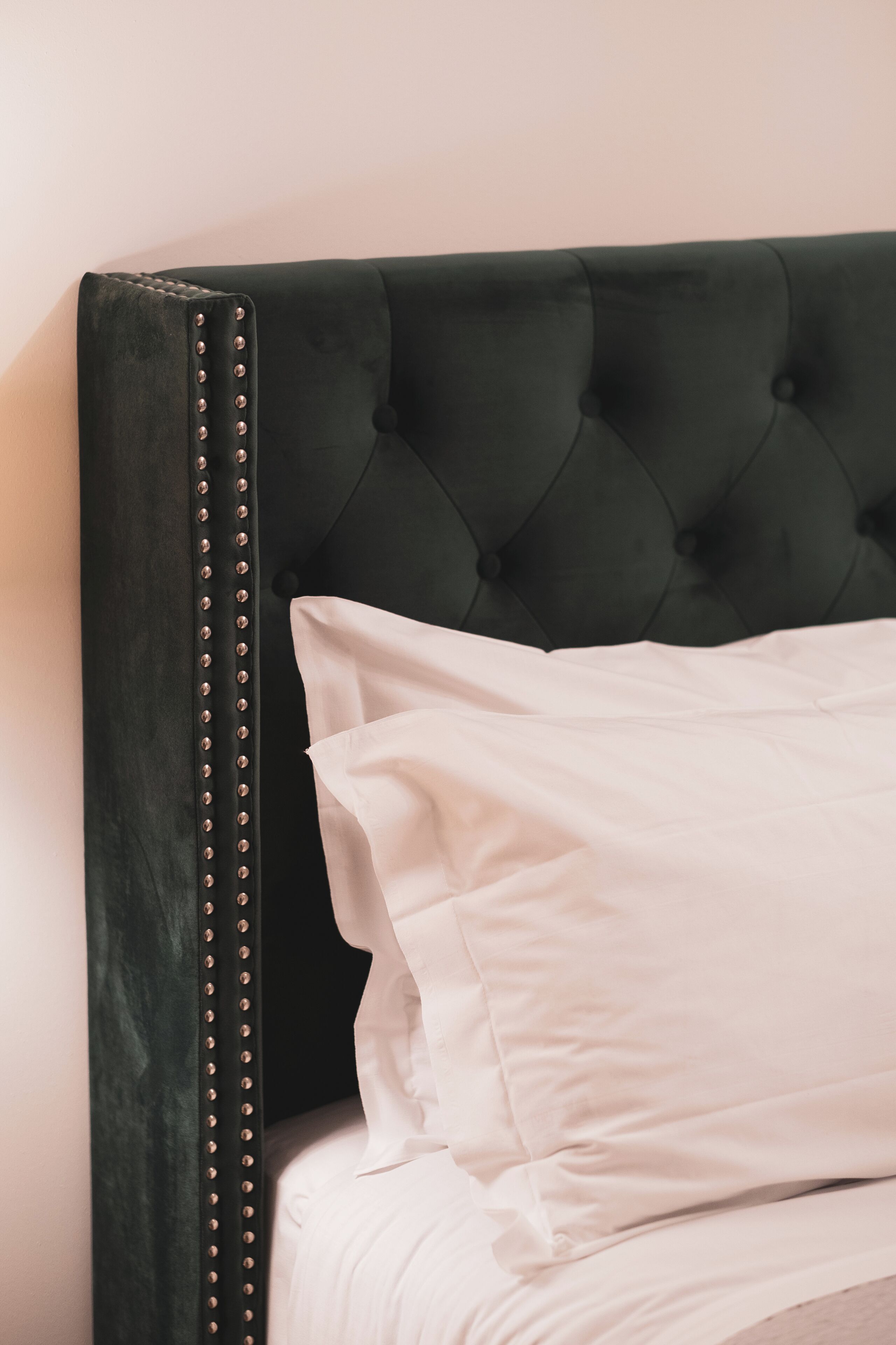 Una cama con cabecera tapizada en verde oscuro y almohada blanca.
