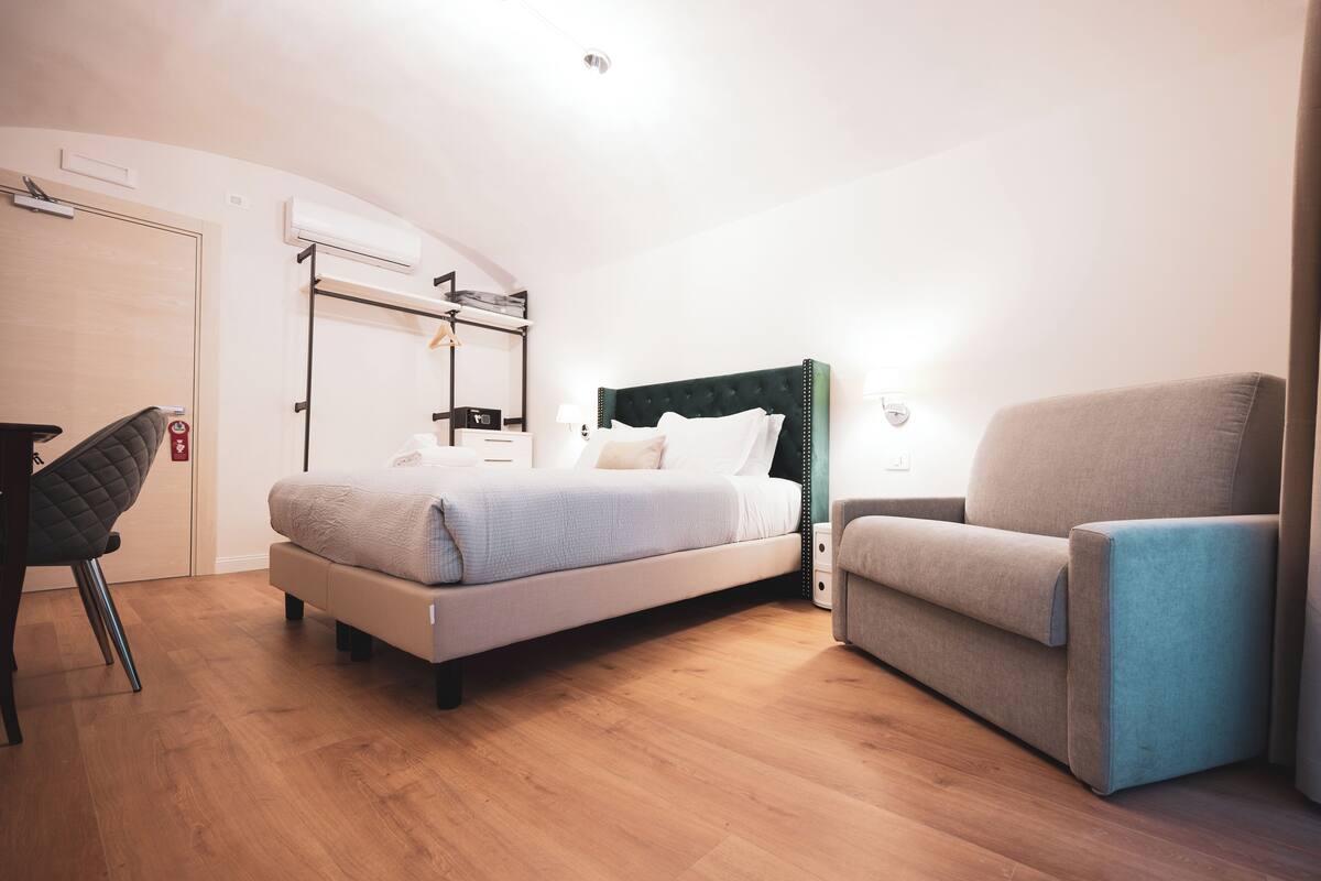Ein modernes Hotelzimmer mit Bett, Sessel, Schreibtisch und Kleiderschrank.