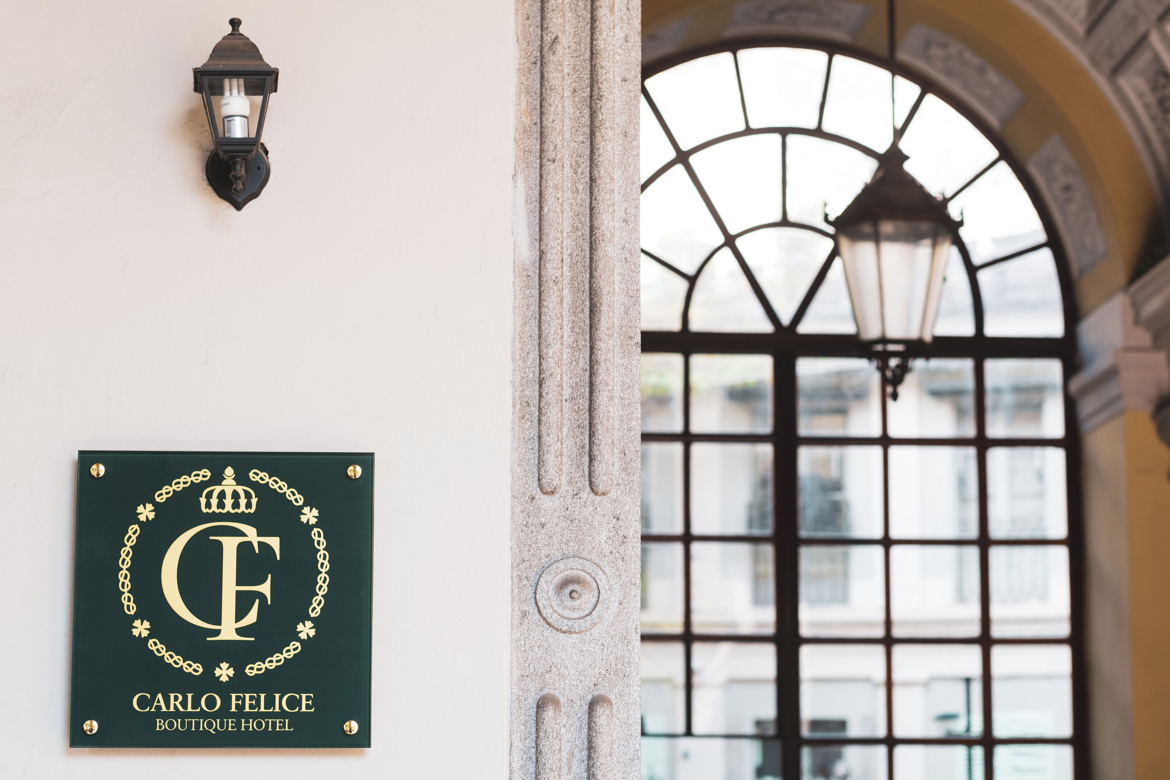 Skilt monteret på væggen for Carlo Felice Boutique Hotel, en stensøjle og et vindue med en dekorativ jernrist.