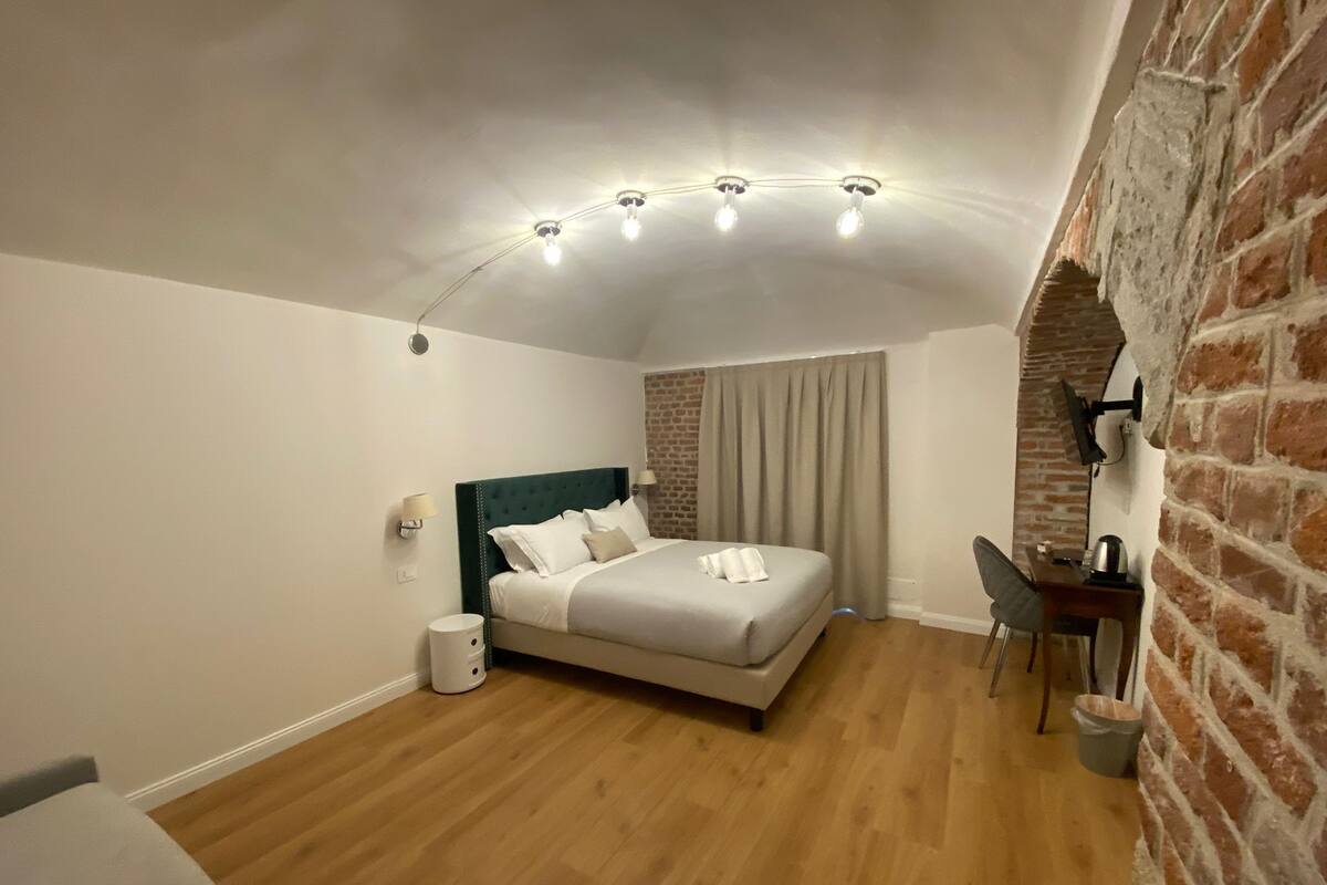 Ein Schlafzimmer mit Bett, Schreibtisch, Stuhl, Lampe und einer Backsteinwand.