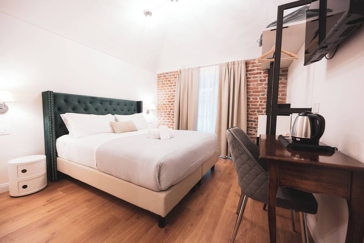 Ein ordentlich eingerichtetes Hotelzimmer mit einem Bett, einem Nachttisch und einem Schreibtisch mit Stuhl.