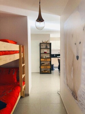 Une pièce avec un lit superposé, une étagère en bois contenant divers objets, un luminaire suspendu et un mur orné d’une fresque représentant un ours.