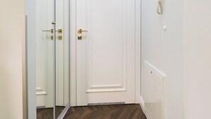 A white door with a brass handle, a mirror reflecting the door, and a white telephone mounted on the wall.