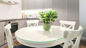 A modern kitchen with grey cabinets, a white dining table with chairs, a hanging light fixture, and a potted plant.