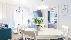 A modern living room with a round dining table, white chairs, a blue sofa, and a chandelier.