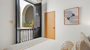 A bedroom with a bed, a wooden door, a window with shutters, and a wall-mounted artwork.