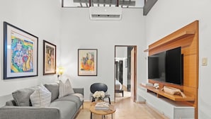 A modern living room with a grey sofa, a coffee table with books and flowers, a TV on a wooden stand, and framed artwork on the walls.