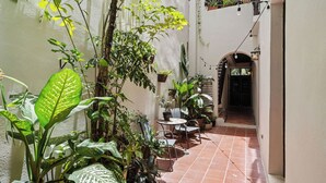 A narrow courtyard with potted plants, a table with chairs, and a tiled floor.